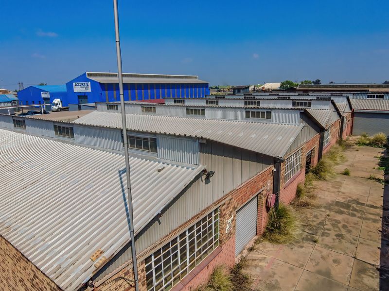 Aerial view of an industrial warehouse complex featuring corrugated metal roofing, brick facades, and paved yard space with roller shutter access.