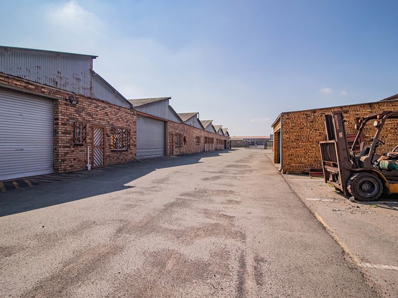 Exterior view of an industrial complex featuring multiple roller shutter doors, face brick construction, and a paved driveway area.