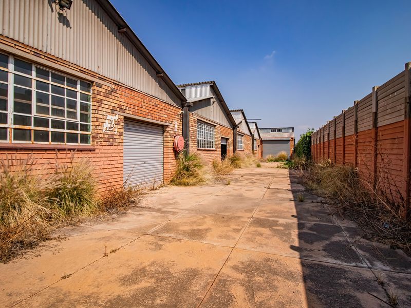 Rear exterior view of an industrial property featuring brick facades, roller shutter doors, and a paved yard area requiring maintenance.