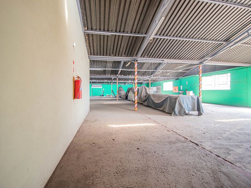 Spacious industrial utility area featuring exposed steel roof trusses, concrete flooring, and painted brick walls, suitable for storage or workshop use.