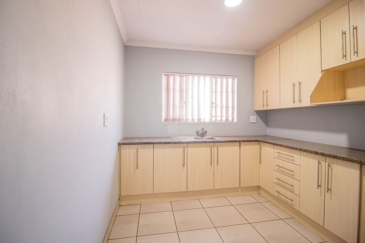 A clean and functional kitchen featuring light wood-tone cabinetry, laminate countertops, a stainless steel sink, and neutral tiled flooring.