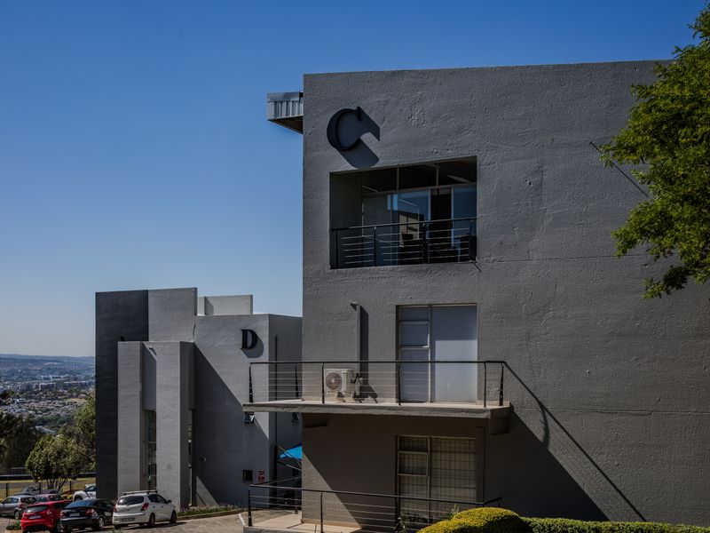 Modern multi-story office building facade featuring grey concrete finish, private balconies with metal railings, and an integrated air conditioning unit.
