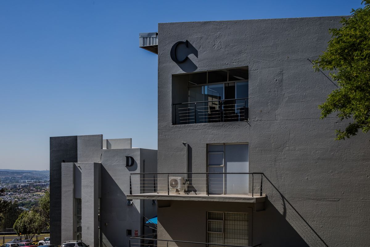 Modern multi-story office building facade featuring grey concrete finish, private balconies with metal railings, and an integrated air conditioning unit.
