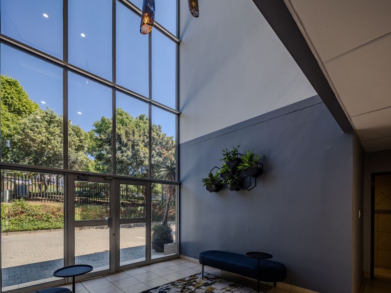 A bright and modern office entrance featuring a double-volume glass facade, tiled flooring, and a high vaulted ceiling, creating an inviting and professional atmosphere.