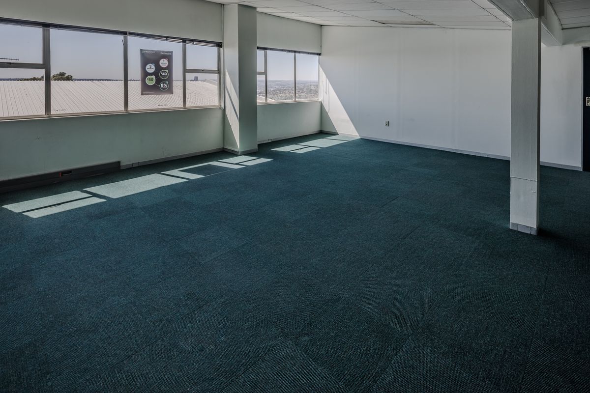 An empty, open-plan office space featuring large windows, suspended ceilings, and carpeted flooring, offering a bright and versatile workspace.