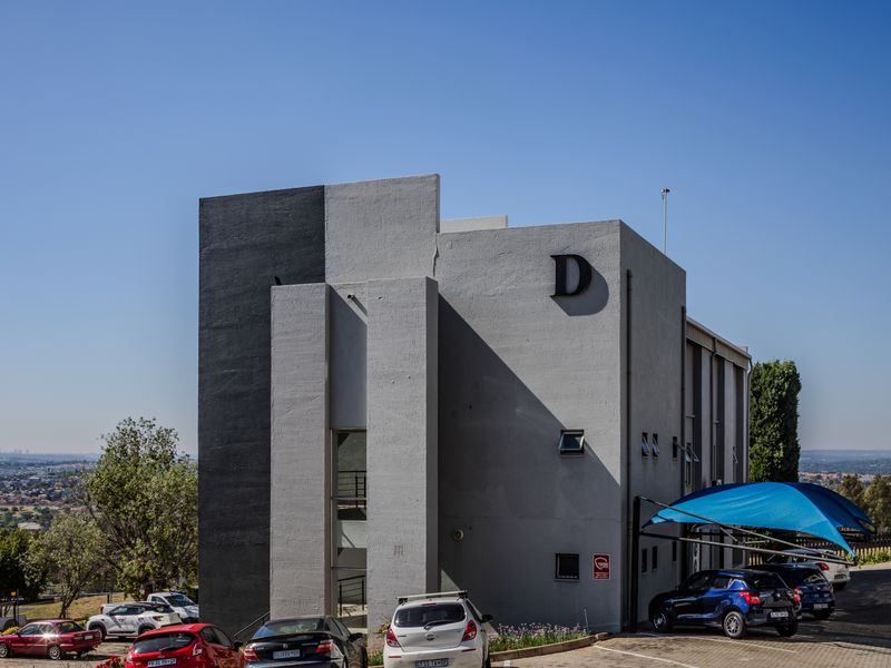 A modern office building exterior featuring a contemporary grey and black facade with dedicated paved parking and shade cloth carports.
