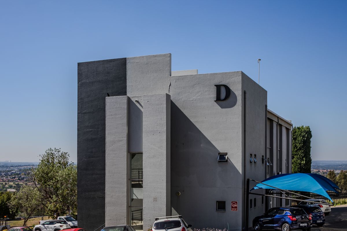 A modern office building exterior featuring a contemporary grey and black facade with dedicated paved parking and shade cloth carports.