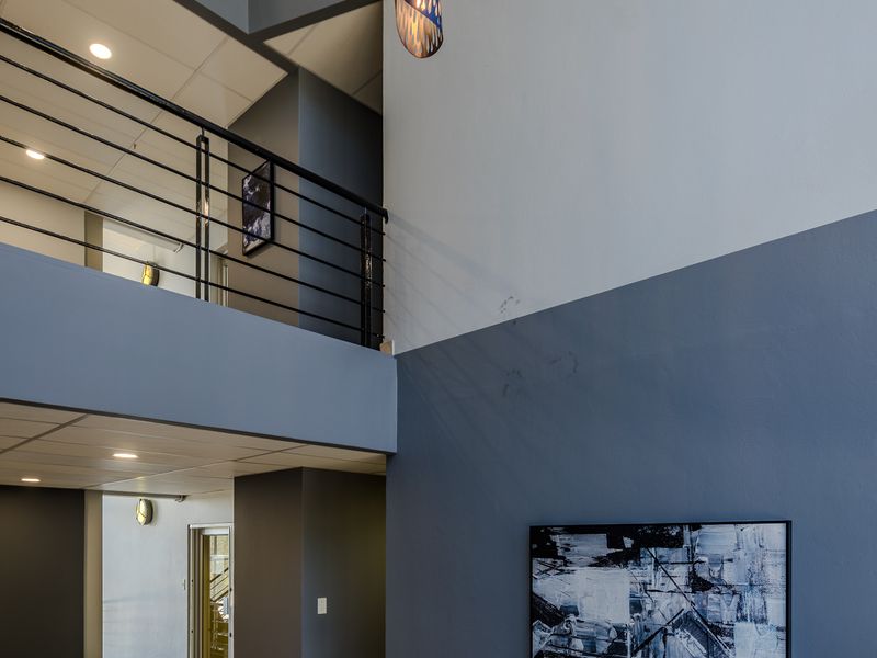 A modern, double-volume office entrance lobby featuring tiled floors, a metal balustrade, and contemporary pendant lighting.