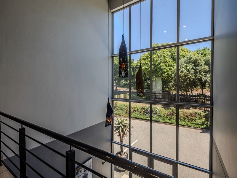 A bright, double-volume office entrance featuring expansive floor-to-ceiling windows, a modern metal balustrade, and contemporary pendant lighting overlooking the exterior parking area.