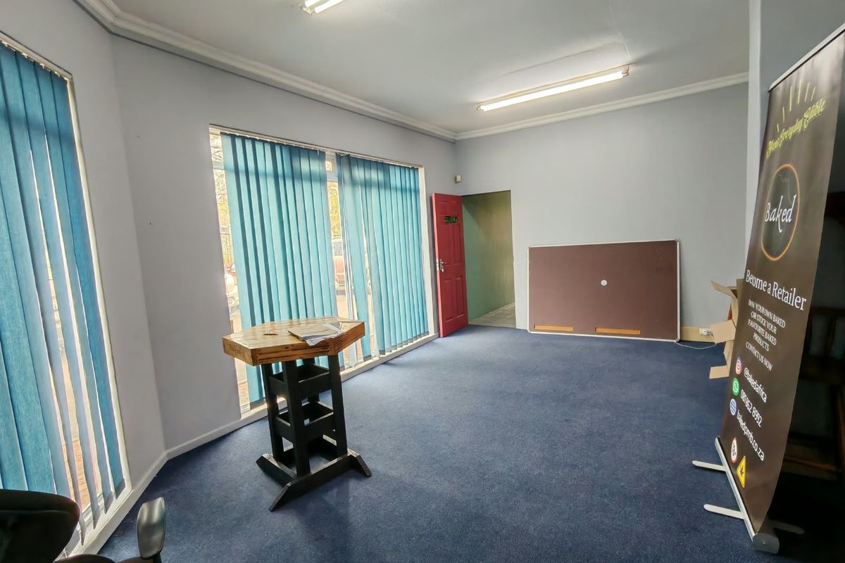 An open, vacant room featuring blue carpeting, vertical window blinds, and fluorescent ceiling lighting, suitable for use as a living area or office space.