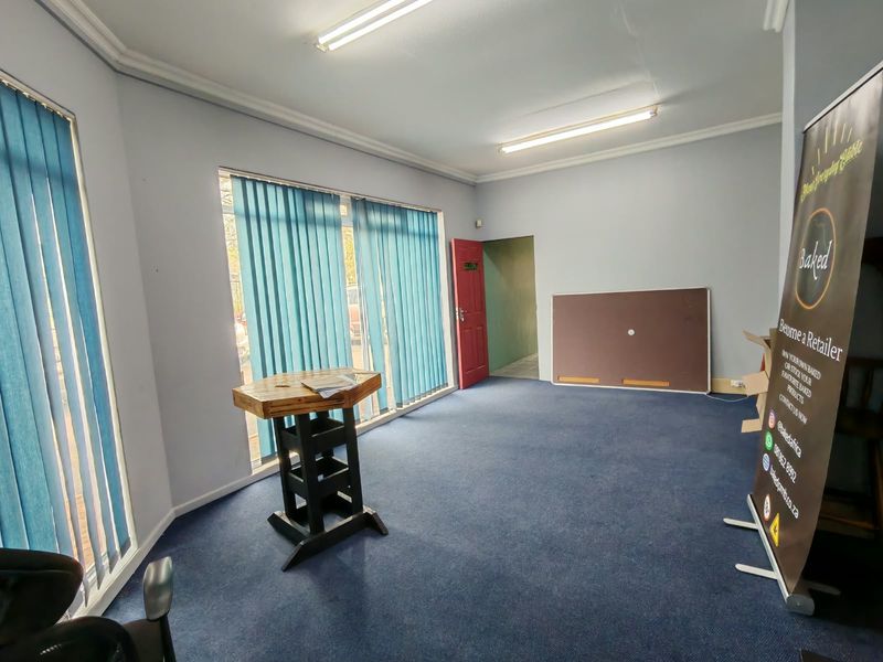 An open, vacant room featuring blue carpeting, vertical window blinds, and fluorescent ceiling lighting, suitable for use as a living area or office space.