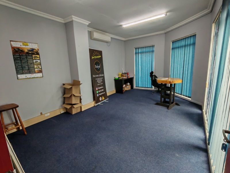 A functional office space featuring blue carpeting, vertical window blinds, and a wall-mounted air conditioning unit.