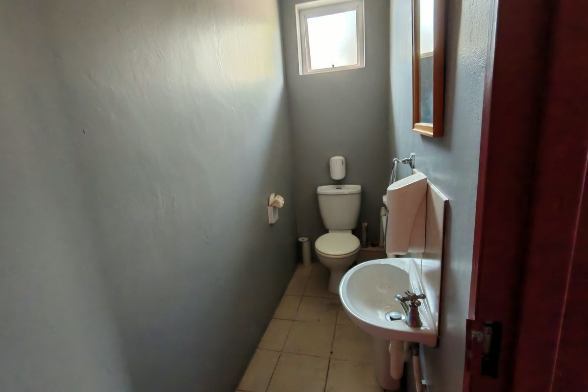 A compact guest bathroom featuring a pedestal basin, toilet, and tiled flooring, requiring minor cosmetic updates to improve its overall aesthetic.