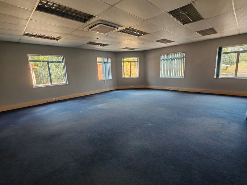 A spacious, empty office area featuring a suspended ceiling with recessed lighting, ducted air conditioning, and large windows with vertical blinds.