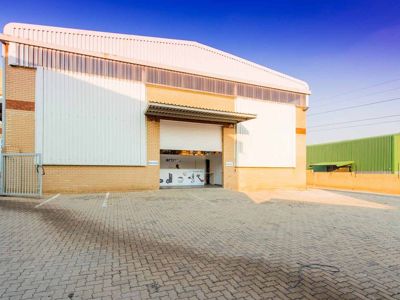 Industrial warehouse exterior featuring a paved driveway, brick and metal cladding facade, and a secure roller shutter entrance.