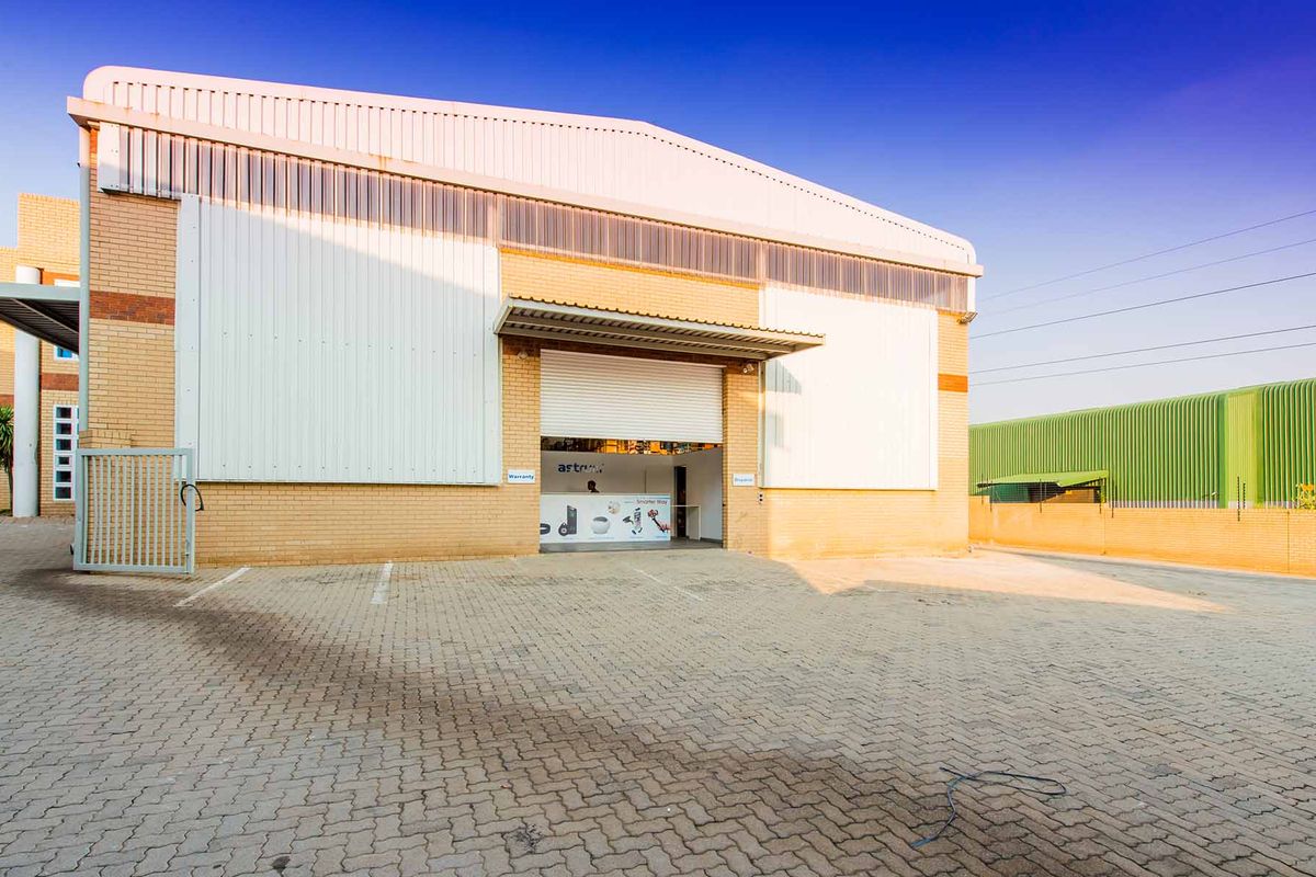 Industrial warehouse exterior featuring a paved driveway, brick and metal cladding facade, and a secure roller shutter entrance.