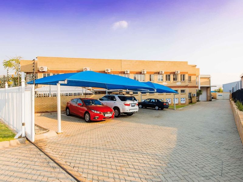 Industrial property exterior featuring a paved driveway, shade cloth carports, and brick building facade with wall-mounted air conditioning units.