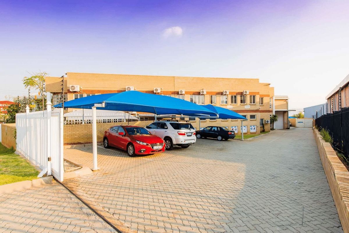 Industrial property exterior featuring a paved driveway, shade cloth carports, and brick building facade with wall-mounted air conditioning units.