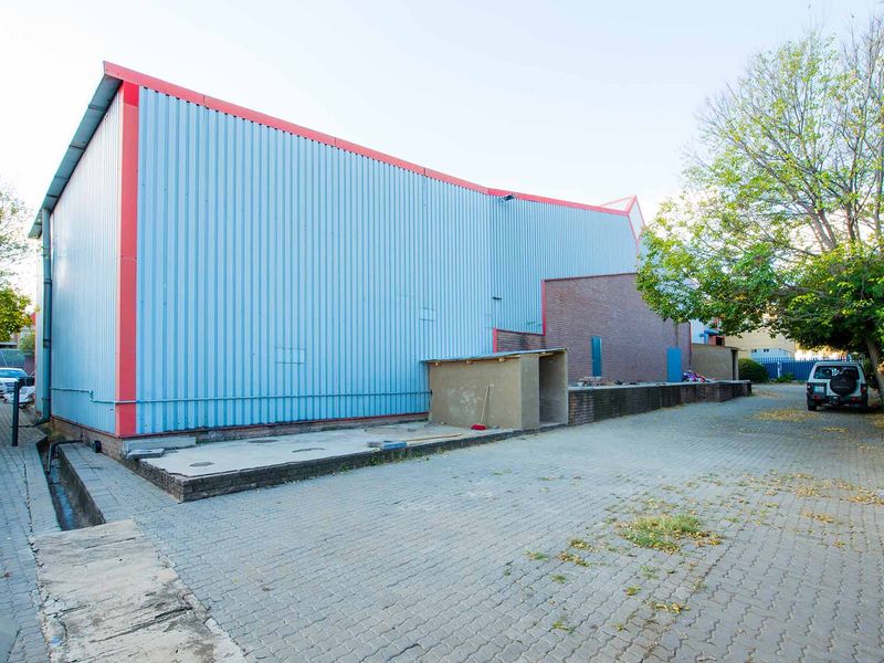 Rear exterior view of an industrial warehouse featuring corrugated metal cladding, brickwork sections, and a paved driveway area.