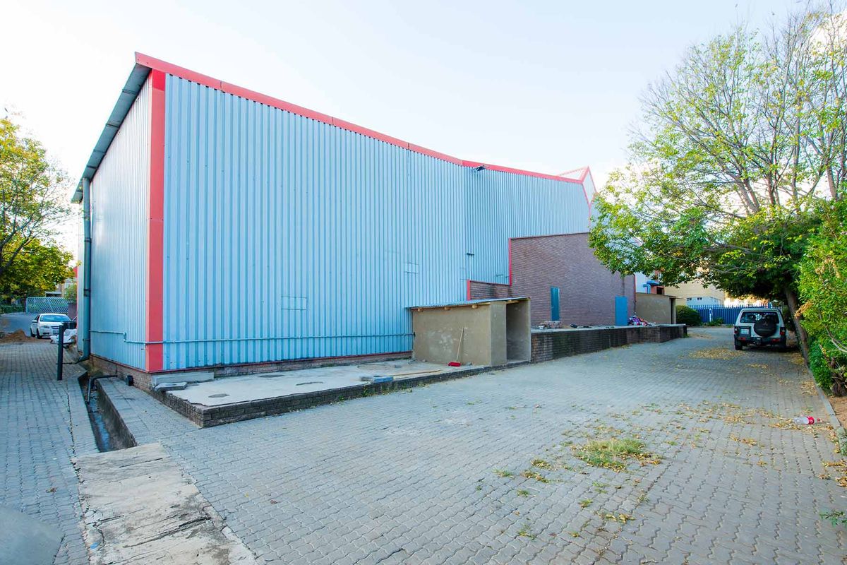 Rear exterior view of an industrial warehouse featuring corrugated metal cladding, brickwork sections, and a paved driveway area.