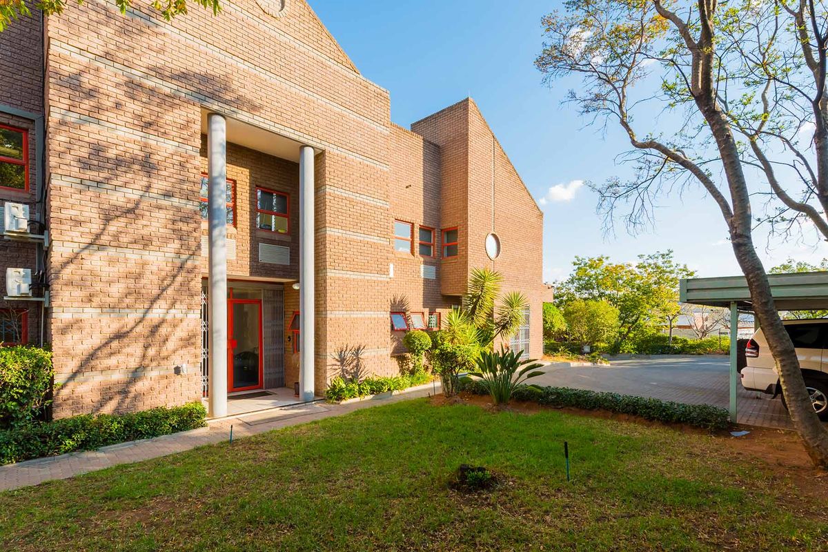 Front elevation of an industrial brick building featuring a covered entrance, paved driveway, and an adjacent carport area with established garden surroundings.
