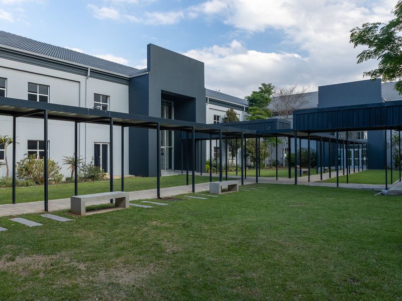 A well-maintained office building exterior featuring a landscaped courtyard with a covered walkway and integrated concrete seating areas.
