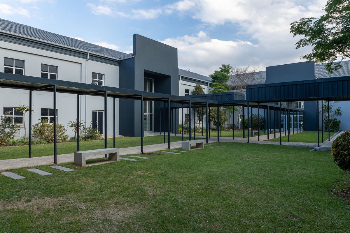 A well-maintained office building exterior featuring a landscaped courtyard with a covered walkway and integrated concrete seating areas.