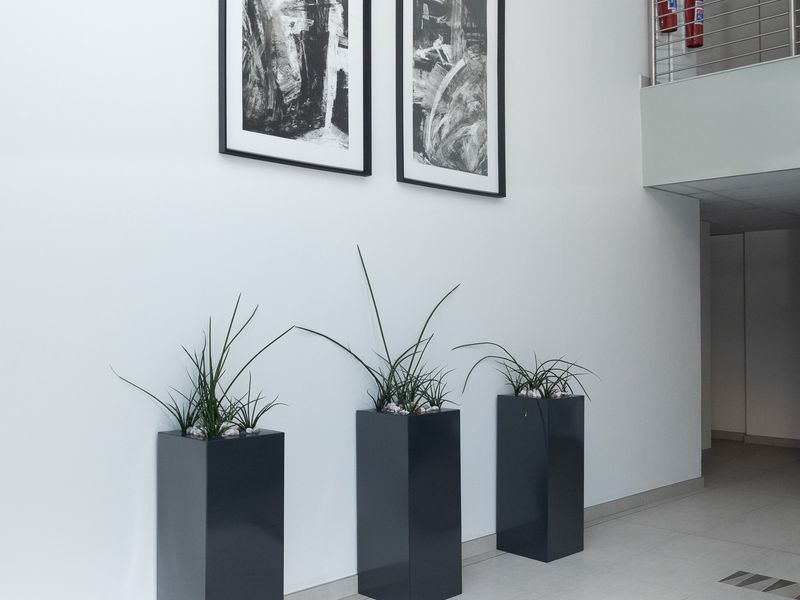 A clean, modern office hallway featuring tiled flooring, a stainless steel balustrade, and integrated fire safety equipment.