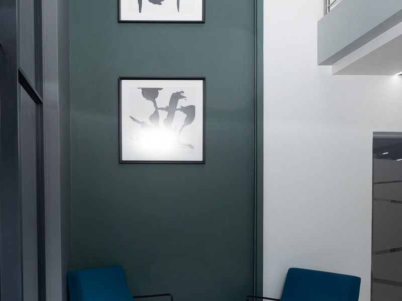 Modern double-volume office entrance foyer featuring a striking dark green accent wall, tiled flooring, and a sleek stainless steel balustrade.