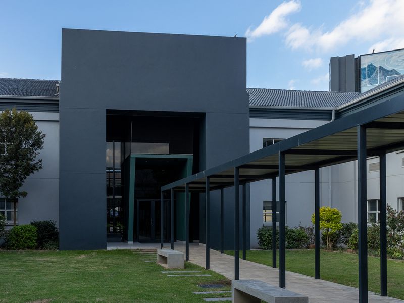 Modern office building entrance featuring a prominent dark facade, a covered pedestrian walkway, and well-maintained landscaped grounds.