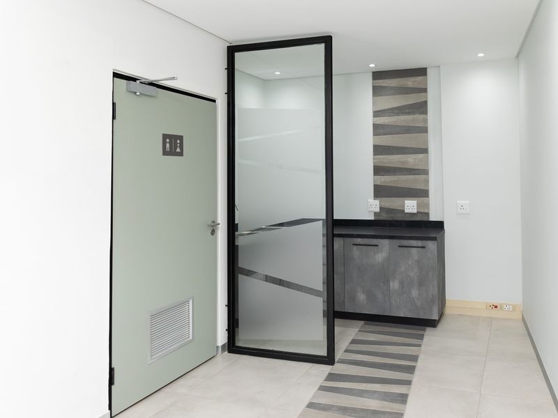 Modern office kitchenette area featuring sleek built-in cabinetry, stone countertop, and a contemporary glass partition with integrated lighting.