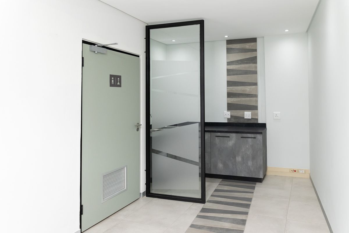 Modern office kitchenette area featuring sleek built-in cabinetry, stone countertop, and a contemporary glass partition with integrated lighting.