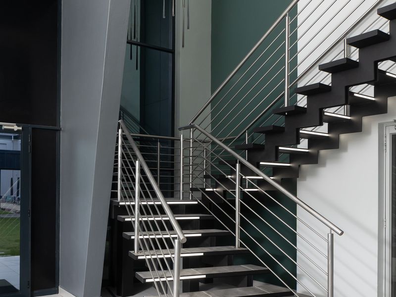 Modern office entrance featuring a contemporary staircase with stainless steel balustrades, tiled flooring, and high ceilings with feature pendant lighting.