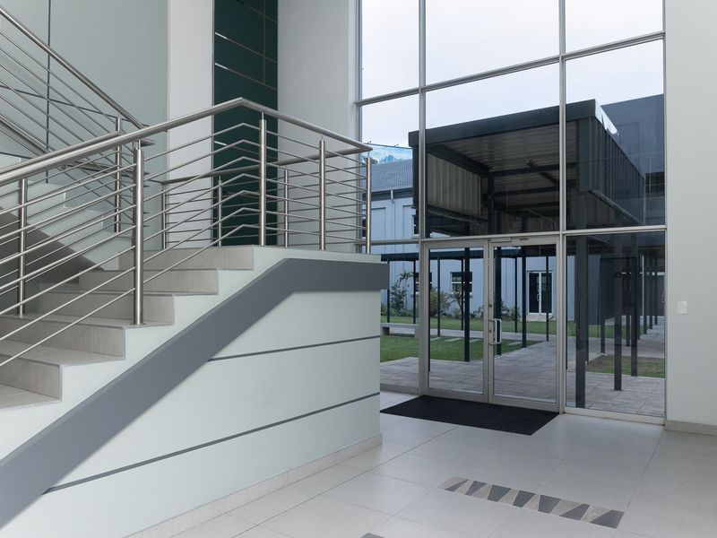 Modern office entrance featuring a tiled staircase with stainless steel balustrades and a full-height glass facade providing natural light and outdoor views.