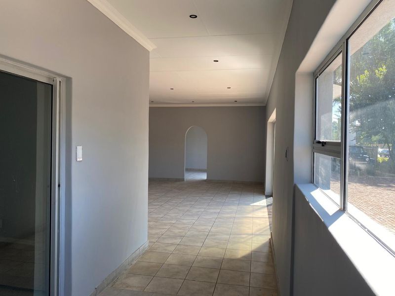 A bright, empty hallway featuring neutral grey walls, tiled flooring, recessed downlighting, and an arched transition leading into an adjacent living space.