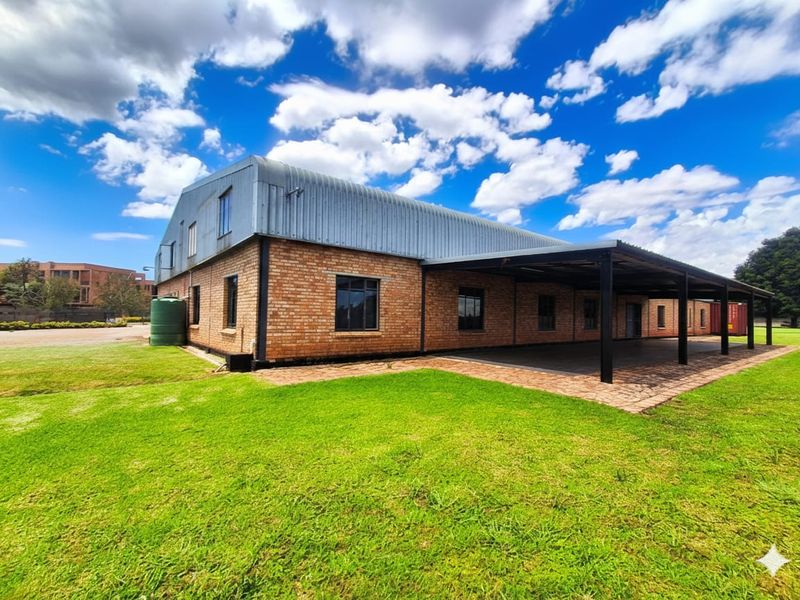Rear view of a brick building featuring a large covered patio area, corrugated metal roofing, and an external water storage tank set on a lawn.