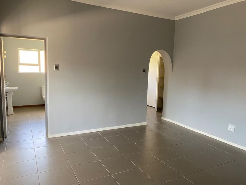 An empty living area featuring neutral grey walls, tiled flooring, and an archway leading to a bathroom and storage space.