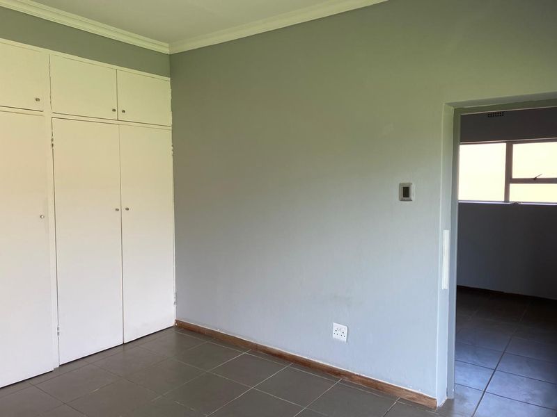 An empty bedroom featuring neutral grey walls, built-in white cupboards, and tiled flooring, offering a clean and versatile space.