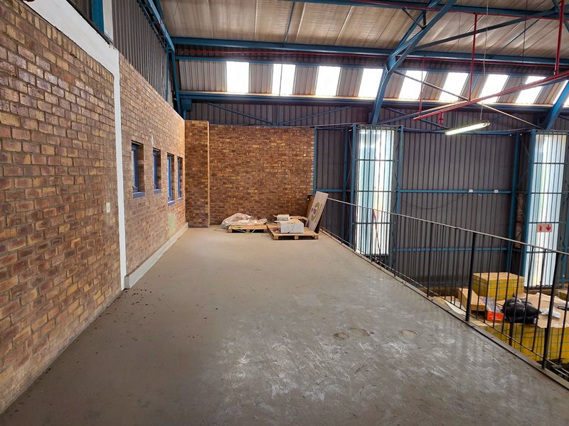 An elevated mezzanine level within an industrial warehouse, featuring exposed brickwork, steel structural elements, and natural light from overhead skylights.