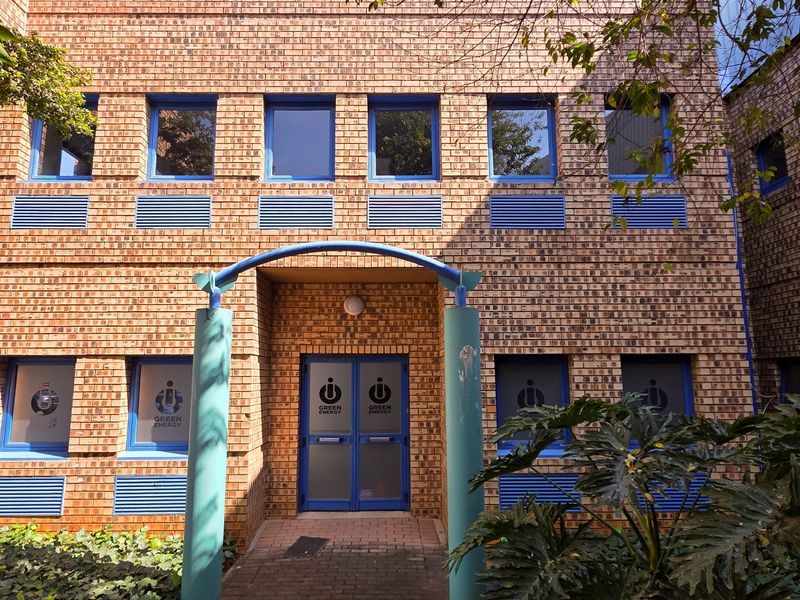 Front facade of a two-story industrial building featuring face brick construction, blue metal window frames, and a covered entrance archway.
