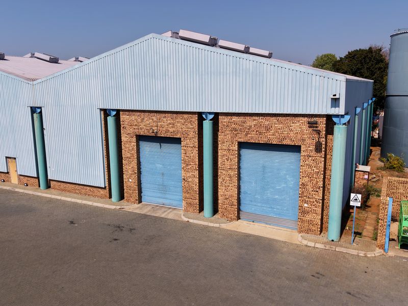 Aerial view of an industrial warehouse facility featuring brick and metal cladding, dual roller shutter doors, and an external water storage tank.
