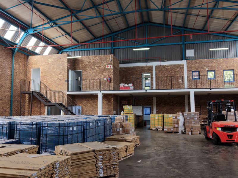 Spacious industrial warehouse featuring high ceilings with exposed steel trusses, a mezzanine level with metal staircase, and durable concrete flooring.