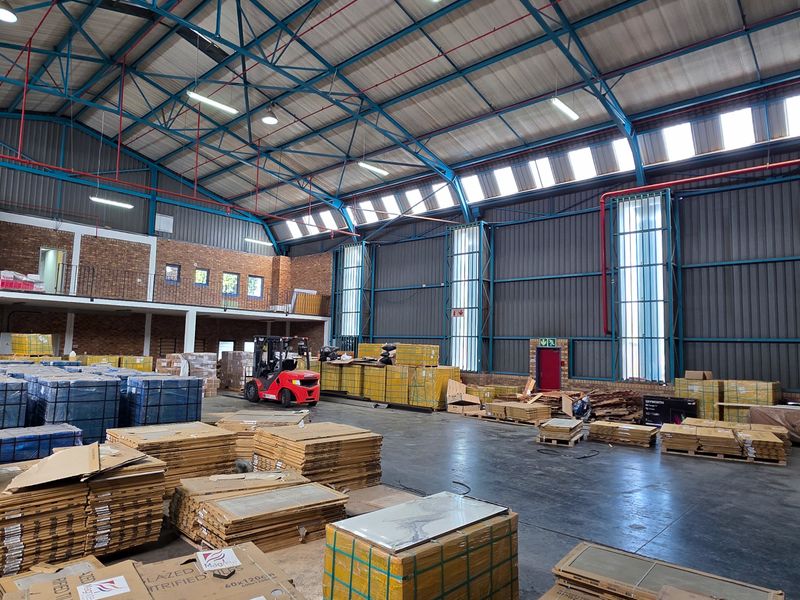 Spacious industrial warehouse featuring high ceilings with exposed steel trusses, brick walls, concrete flooring, and a functional mezzanine level for storage or office use.