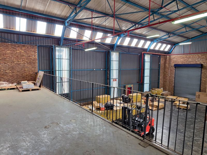 Spacious industrial warehouse featuring a mezzanine level, exposed steel roof trusses, roller shutter doors, and durable concrete flooring.