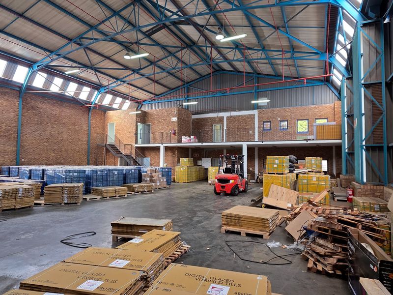 Spacious industrial warehouse featuring high ceilings with exposed steel trusses, concrete flooring, brick walls, and a functional mezzanine level for additional storage or office space.