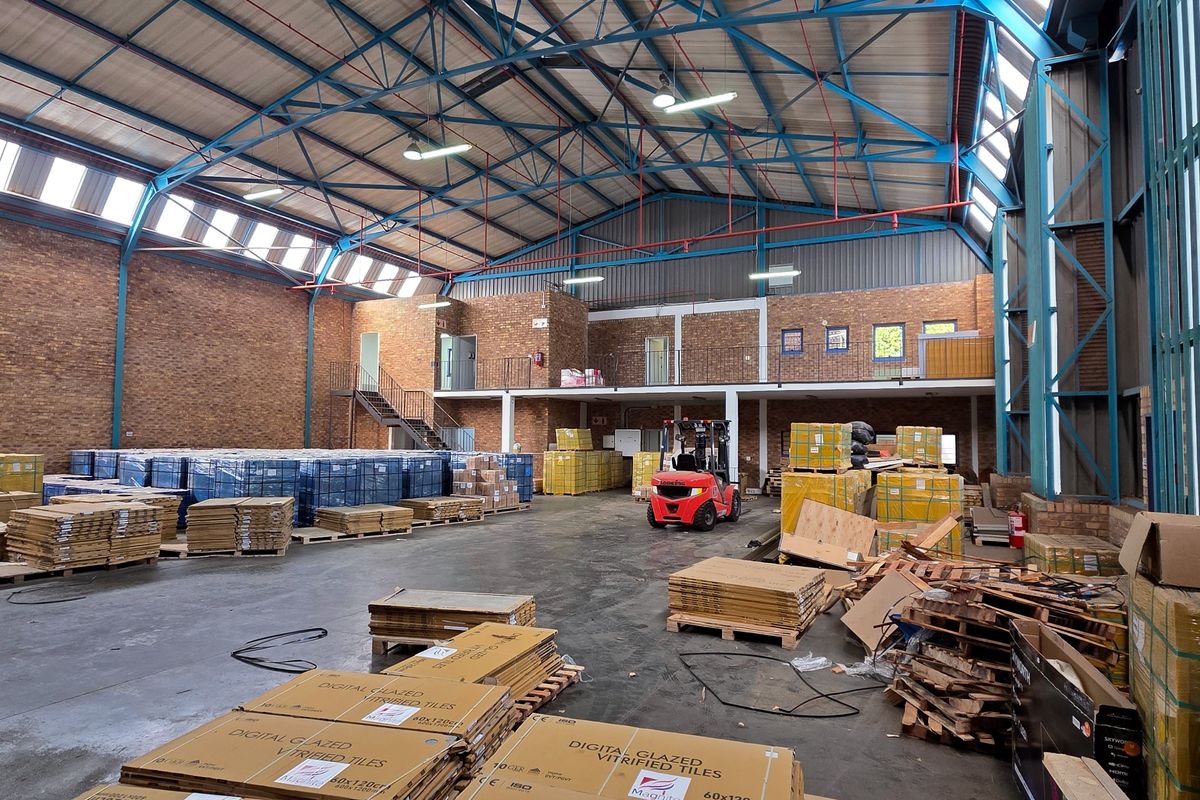 Spacious industrial warehouse featuring high ceilings with exposed steel trusses, concrete flooring, brick walls, and a functional mezzanine level for additional storage or office space.
