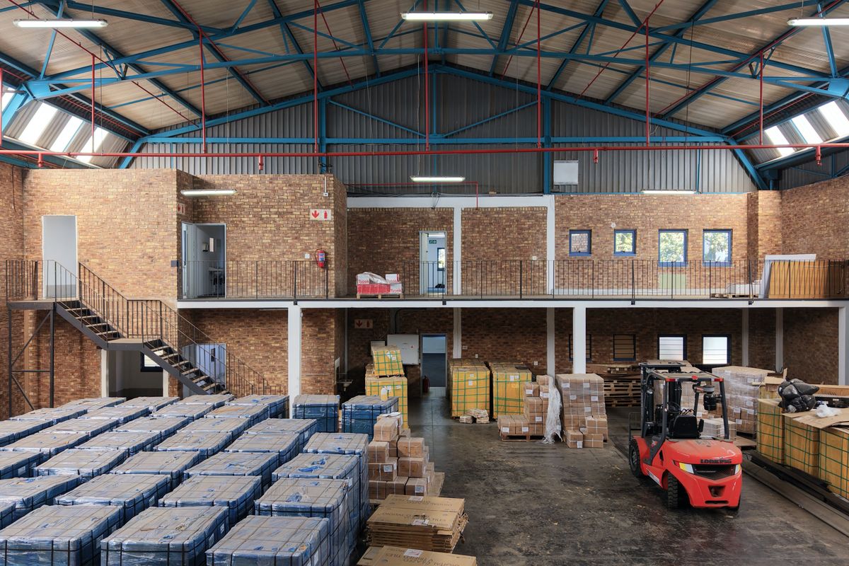 Spacious industrial warehouse featuring a mezzanine level, exposed steel roof trusses, brick walls, and high-clearance ceilings suitable for storage or manufacturing operations.