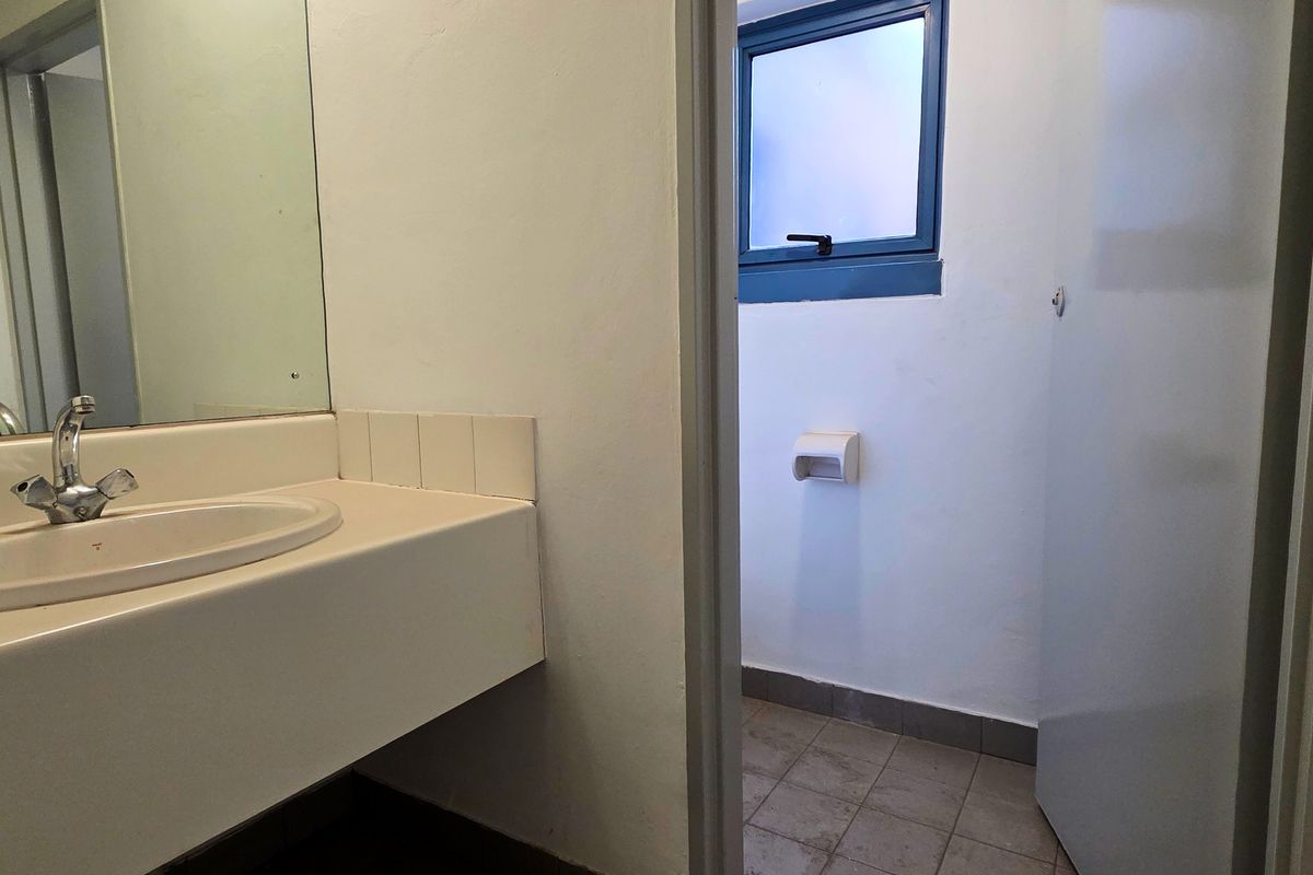 A functional industrial-style bathroom featuring a vanity basin, wall-mounted mirror, and tiled flooring, requiring cosmetic updates to improve its overall condition.