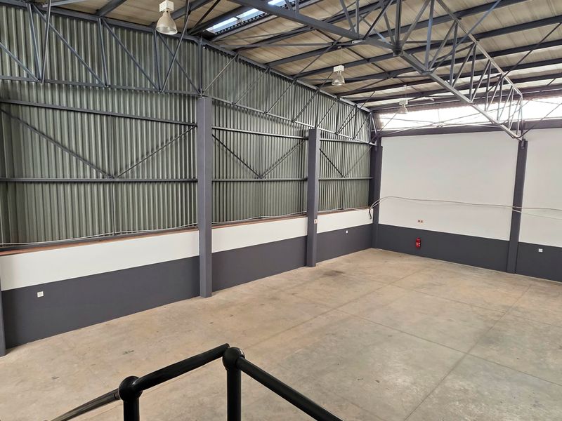 Spacious industrial warehouse unit featuring high ceilings with exposed steel trusses, durable concrete flooring, and corrugated metal wall cladding.