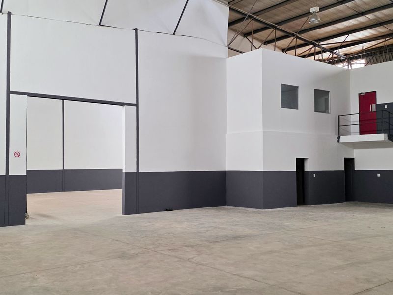 Spacious industrial warehouse unit featuring high ceilings with exposed steel trusses, concrete flooring, and a mezzanine level with integrated office space and staircase.
